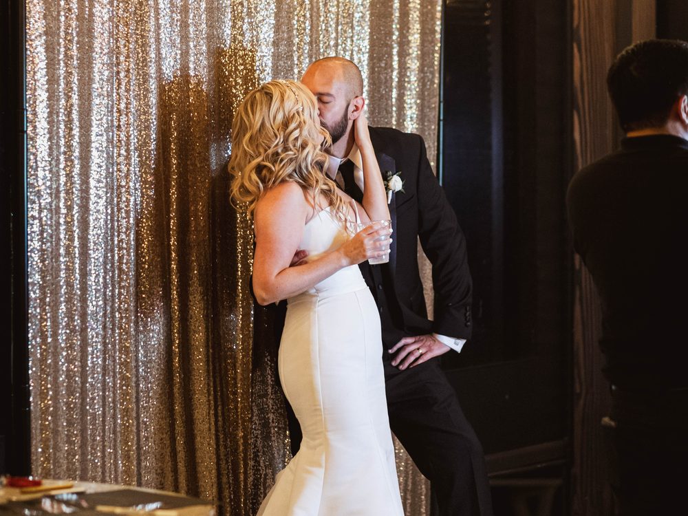Newlyweds kissing in front of a gold sequin backdrop